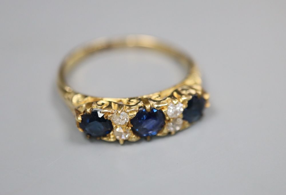 An 18ct, three stone sapphire and four stone diamond set dress ring, with carved setting, size O, gross 3.6 grams.